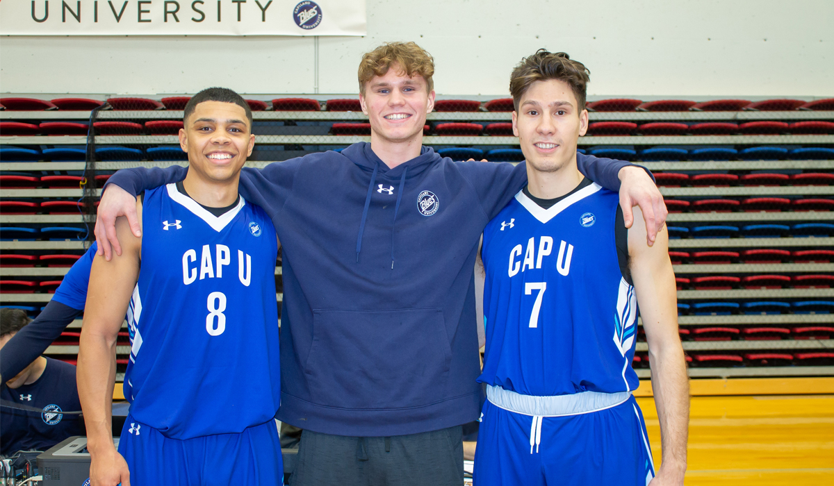 Playing their final home games at CapU, Blues guards CJ Campbell (left) and Marko Cosic (right) flank former Blues forward Sam Bailey on Senior Night.